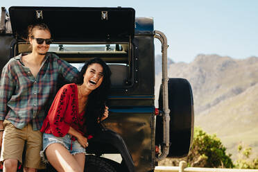 Beautiful woman standing with her boyfriend and laughing. Couple standing leaning to the car outdoors and looking happy. - JLPSF21155