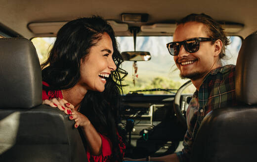 Rückansicht eines jungen Paares auf einer Autoreise: Ein lächelnder Mann und eine lächelnde Frau, die in einem Auto sitzen und zurückblicken. - JLPSF21171