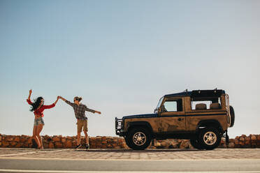 Couple dancing in front of their car. Man and woman enjoying a summer vacation road trip. - JLPSF21173