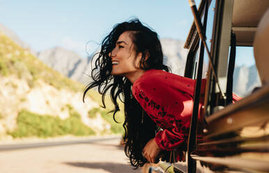 Beautiful caucasian woman looking out of the car and smiling on road trip. Woman having fun while traveling by a car. - JLPSF21185