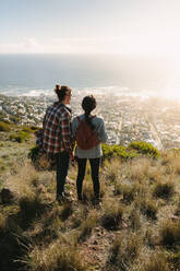 Rear view of young man and woman standing on cliff and looking at view on a summer day. Young couple on hiking trip. - JLPSF21201