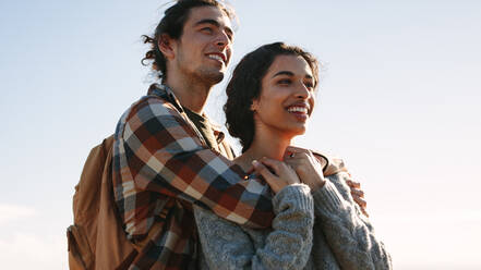 Young man with backpack standing with his woman looking away and smiling. Loving couple looking at a view and with smile on face. - JLPSF21206