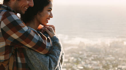 Nahaufnahme eines jungen verliebten Paares, das zusammen im Freien steht und den Moment genießt. Mann und Frau umarmen sich und schauen auf eine Aussicht. - JLPSF21212