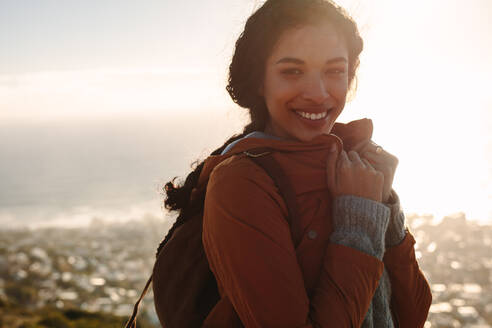 Porträt lächelnd bei strahlendem Sonnenschein an einem Wintertag. Frau im Urlaub steht im Freien und trägt eine warme Jacke. - JLPSF21222
