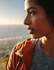 Close up Portrait einer schönen afrikanischen Frau in Pullover und Jacke, die im Freien steht und wegschaut. Gesicht einer jungen afrikanischen Frau, die an einem Wintertag im Freien wegschaut. - JLPSF21224