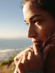 Beautiful woman standing on mountain on a winter day and looking at sea. African female outdoors on winter vacation. Close up of female face wearing warm clothing. - JLPSF21229