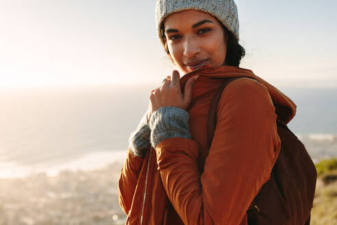 Porträt einer jungen afrikanischen Frau in warmer Kleidung, die an einem Wintertag auf einer Klippe steht. Frau auf Wanderschaft in der Natur. - JLPSF21233