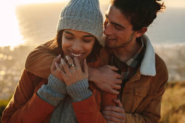 Close up portrait of affectionate young couple on winter holiday. Handsome young man embracing his girlfriend from behind in a winter day. - JLPSF21236