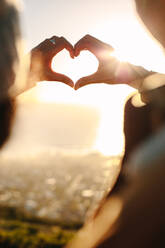 Close up of young couple in love making a heart with their fingers in bright sunlight. Romantic couple gesturing a finger heart. - JLPSF21238