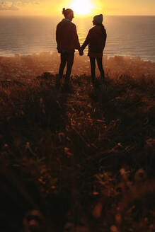 Silhouette of young couple in love standing together on the mountain peak at sunset. Love couple on peak looking at each other during sunset. Vertical shot. - JLPSF21254