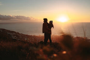 Romantisches Paar, das sich bei Sonnenuntergang auf einem Berggipfel umarmt. Mann und Frau stehen zusammen auf dem Gipfel mit Meereslandschaft im Hintergrund. - JLPSF21256