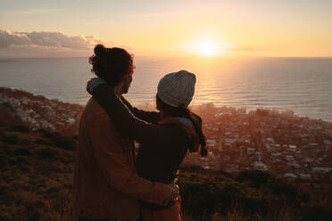 Romantisches Paar, das den Sonnenuntergang über dem Meer von einem Berg aus bewundert. Junger Mann und Frau zusammen auf einem Berggipfel mit einer Meereslandschaft im Hintergrund. - JLPSF21258