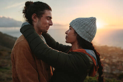Seitenansicht eines schönen jungen Paares, das sich umarmt und verliebt anschaut. Romantisches Paar, das während des Sonnenuntergangs auf einem Berggipfel Zeit miteinander verbringt. - JLPSF21259