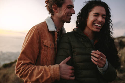Ein reisendes Pärchen steht im Freien und lacht zusammen. Mann und Frau in warmer Kleidung stehen auf einem Berg und genießen den Moment. - JLPSF21266