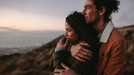 Side view of affectionate couple embracing and looking away. Man and woman together on mountain looking at a view. - JLPSF21272