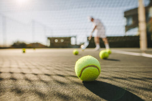 Tennisbälle liegen auf dem Boden auf einem Tennisplatz. Mann spielt Tennis an einem sonnigen Tag mit Tennisbällen auf dem Platz. - JLPSF21285