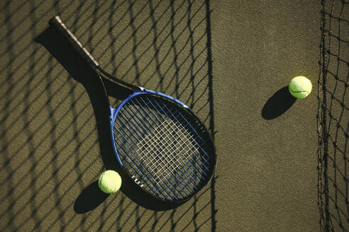 Nahaufnahme eines Tennisschlägers und Bälle, die auf dem Platz liegen. Tennisschläger und Bälle neben einem Netz auf einem Tennisplatz an einem sonnigen Tag. - JLPSF21286