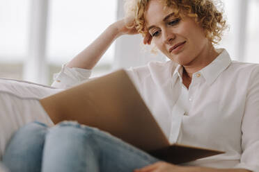 Businesswoman working from home on laptop. Woman sitting comfortably at home on couch with a laptop. - JLPSF21329