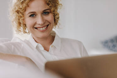 Porträt einer lächelnden Geschäftsfrau, die an einem Laptop arbeitet. Braunhaarige Frau sitzt zu Hause und arbeitet an einem Laptop. - JLPSF21331