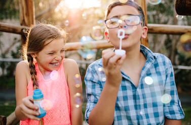 Young boy and girl having fun playing with soap bubbles. Young boy blowing soap bubbles while an excited girl enjoys the bubbles. - JLPSF21333