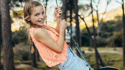 Happy girl swinging on a tyre swing in a park. Girl having fun standing on a tire swing in a park. - JLPSF21334