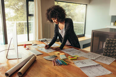 Junge afrikanische Geschäftsfrau, die an einem Projekt arbeitet. Frau arbeitet im Büro zu Hause und schreibt auf einem Diagramm auf einem Tisch. - JLPSF21344
