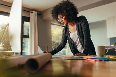 Female designer working on a new project. Woman with curly hair reviewing a design at home office. - JLPSF21345