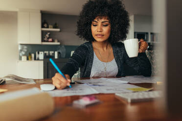 Architektin macht einen Projektplan mit einer Tasse Kaffee in der Hand. Innenarchitektin korrigiert eine Zeichnung, während sie zu Hause im Büro sitzt. - JLPSF21356