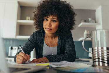 Afrikanische Frau sitzt an ihrem Arbeitstisch und schaut auf den Computerbildschirm, während sie einen Bauplan vorbereitet. Junge Architektin arbeitet an einem neuen Gebäudeplan. - JLPSF21377