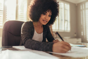 Konzentrierte junge Geschäftsfrau bei der Arbeit an Plänen im Büro. Afrikanische Architektin bei der Arbeit an neuen Entwürfen in ihrem Büro zu Hause. - JLPSF21389