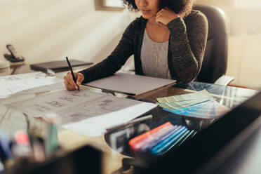 Architektin, die an ihrem Schreibtisch an Hausgrundrissen arbeitet. Frau, die an ihrem Schreibtisch sitzend einen neuen Bauplan vorbereitet. - JLPSF21390