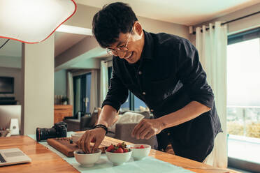 Lächelnde Fotografin, die Essen auf dem Tisch für ein Fotoshooting vorbereitet. Asiatische Fotografin, die Essen für ein Werbe-Fotoshooting vorbereitet. - JLPSF21406