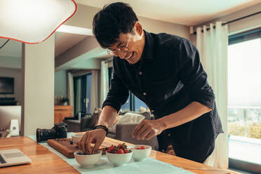 Smiling food photographer styling food on table for shoot. Asian photographer preparing food for advert photoshoot. - JLPSF21406