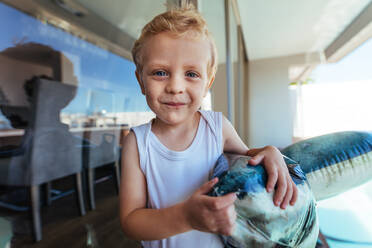 Nahaufnahme eines kleinen Jungen mit einem Spielzeug am Swimmingpool, der ein aufblasbares Spielzeug hält und lächelt. - JLPSF21412