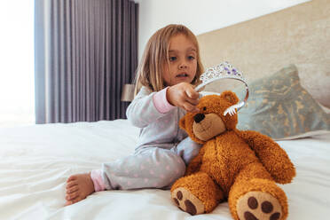 Innocent young girl putting a crown on her teddy bear. Little girl playing with her soft toy. - JLPSF21418