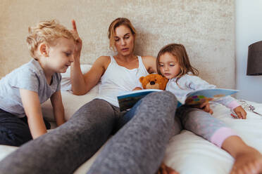 Mutter liest Kindern zu Hause eine Gute-Nacht-Geschichte vor. fürsorgliche Mutter liest Buch für entzückende kleine Kinder auf dem Bett. - JLPSF21423