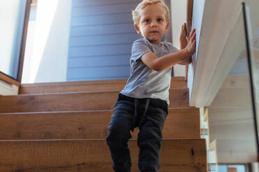 Kleiner Junge geht die Treppe hinunter und stützt sich dabei auf eine Wand. Kleines Kind geht allein die Treppe zu Hause hinunter. - JLPSF21428