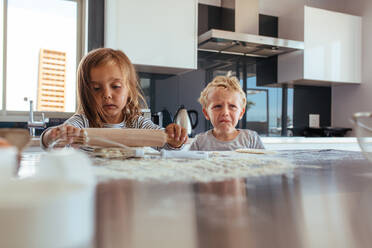 Unschuldiges kleines Mädchen mit Nudelholz und weinender Junge in Küche. Kleine Kinder backen Kekse in Küche. - JLPSF21455