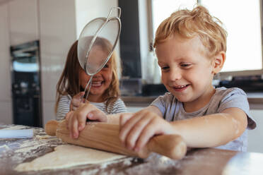 Kinder backen Kekse und haben Spaß in der Küche. Kleiner Junge und Mädchen bereiten Kekse auf dem Küchentisch vor. - JLPSF21456