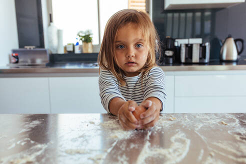 Unschuldiges kleines Mädchen bricht ein Ei mit Mehl auf dem Küchentisch auf. Kleines Mädchen backt in der Küche zu Hause. - JLPSF21459