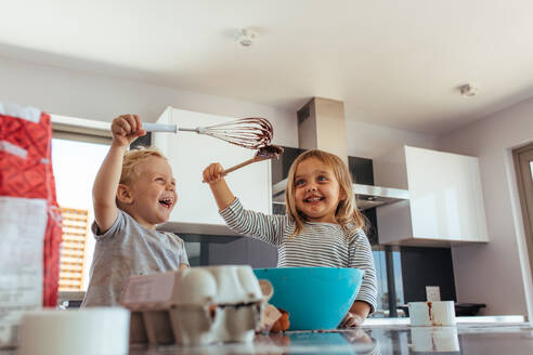 Niedlicher kleiner Junge und Mädchen kämpfen mit Schneebesen und Spachtel beim Mischen von Teig in einer Schüssel. Geschwister genießen das Backen in der heimischen Küche. - JLPSF21468