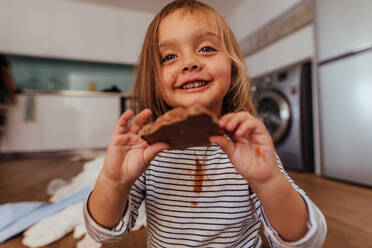 Schönes Mädchen zeigt eine Schokolade, die sie isst. Kleines Mädchen isst ihre Lieblingsschokolade zu Hause. - JLPSF21489