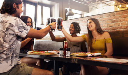 Multi-ethnic group of people toasting soft drinks at a cafe. Men and women sitting inside a restaurant toasting drinks. - JLPSF21495