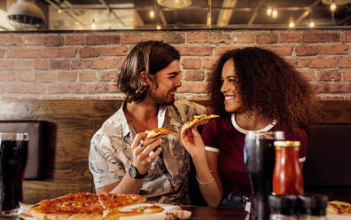 Porträt eines jungen Mannes und einer Frau, die in einem Fast-Food-Restaurant sitzen und eine Pizza essen. Fröhliches Paar, das in einem Café Pizza isst. - JLPSF21498
