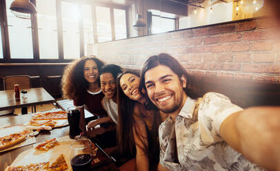 Junger Mann macht ein Selfie mit Freunden in einem Café. Eine Gruppe multiethnischer Freunde in einem Restaurant hält einen Moment mit der Kamera fest. - JLPSF21506