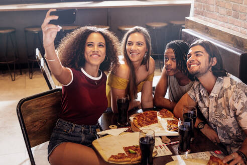 Junge Frau, die ein Selfie mit Freunden im Restaurant macht. Gruppe multiethnischer Freunde im Café, die ein Selfie mit ihrem Smartphone machen. - JLPSF21509