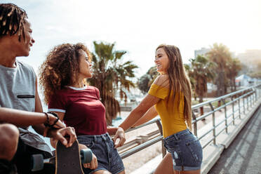 Beautiful woman standing by a railing outdoors with friends. Multiracial friends together outdoors with a skateboard. - JLPSF21514