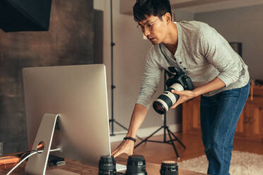 Männlicher Fotograf in seinem Studio mit Kamera und Desktop-Computer, der seinen Computer für das Shooting einrichtet. - JLPSF21523