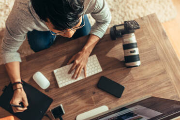 Draufsicht auf einen Fotografen, der seine Fotos in seinem Studio bearbeitet. Ein Fotograf bearbeitet seine Fotos nach einem Fotoshooting mit einem Grafiktablett und einem Stylus-Stift. Fokus auf den Fotografen. - JLPSF21529