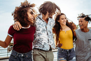 Four young people walking outdoors together. Group of multi-ethnic men and women having fun outdoors. - JLPSF21531